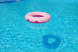 Pink floatation device casting a shadow on the bottom of the blue pool.