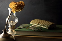 Arrangement with old books, spectacles, case, glass oil lamp and dead rose