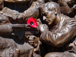 Bronze sculptured war memorial with a red poppy pinned to it