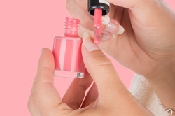 Young woman applying a pink nail polish to her finger
