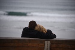 Two people embraced on a bench over looking the beach and surf