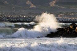 Big waves pound in Oxnard, California. Seagull can be seen sitting on the harbor rocks in the background