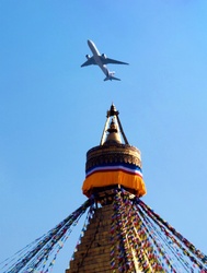 A commercial airliner, just taken off from Kathmandu International Airport, seen from by the Boudanath stupa