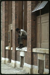 A Black man who is jobless sits on the windowsill of a building in a high crime areaâ¦