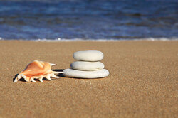 Pebbles and shell in sand with ocean in background 