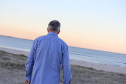 Man in blue shirt walking on the beach looking down